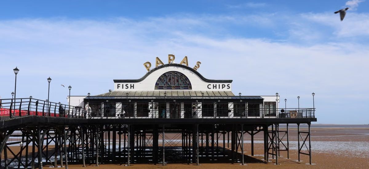 Classic view of Cleethorpes Pier with a fish and chips shop under a blue sky.
