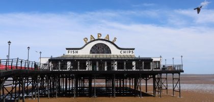 Classic view of Cleethorpes Pier with a fish and chips shop under a blue sky.