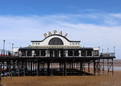 Classic view of Cleethorpes Pier with a fish and chips shop under a blue sky.
