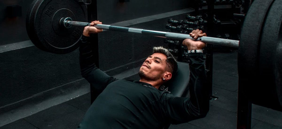 Man performing bench press with heavy barbell in a gym setting, focusing on strength training.