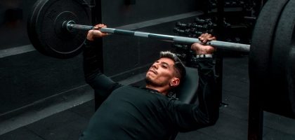 Man performing bench press with heavy barbell in a gym setting, focusing on strength training.